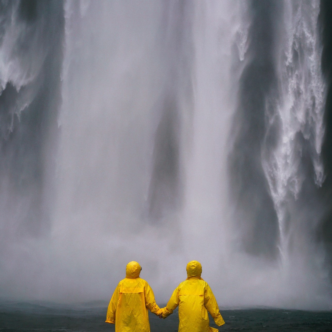 Due ragazzi con impermeabile giallo a mano a mano verso una cascata