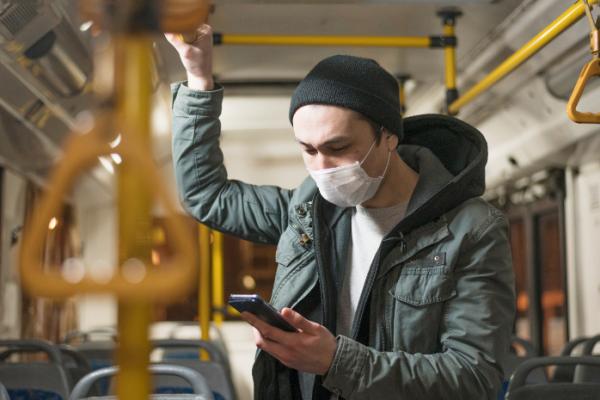 Un ragazzo con indosso una mascherina controlla il telefono, mentre viaggio sul bus.